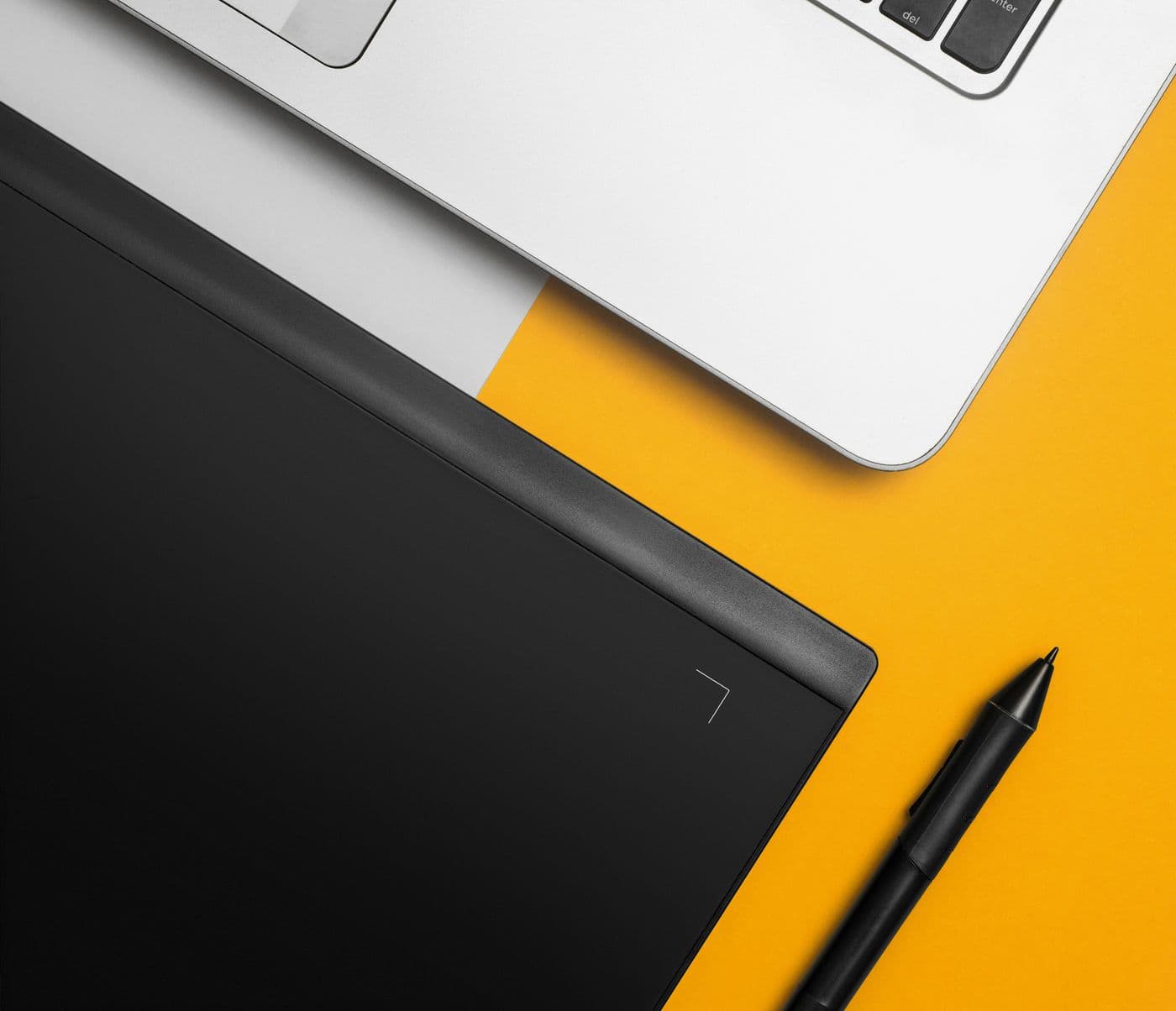 Tablet graficzny z rysikiem obok laptopa na pomarańczowym blacie